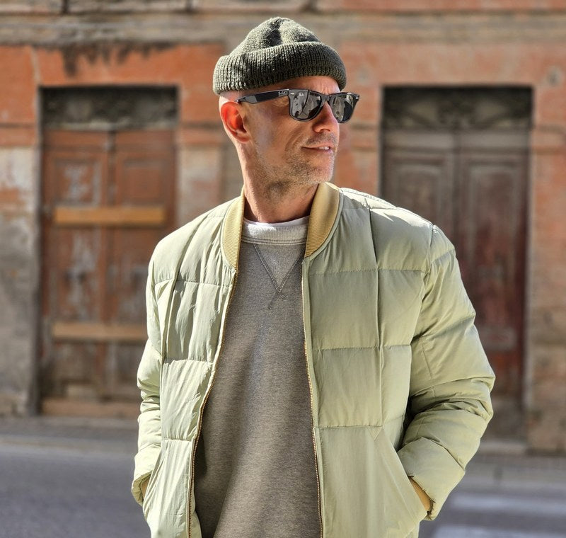 Hombre en la calle con un plumífero Chesapeake's verde salvia y gorro; al lado, un hombre con chaquetón Chesapeake's y gorro naranja.